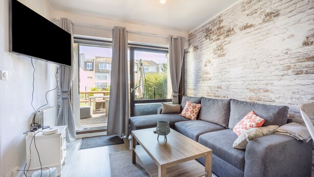 A modern living room with a grey sofa, a wooden coffee table, and a flat-screen TV mounted on the wall. - Galene - Appt avec jardin à 700 m de la Plage (Courseulles-sur-Mer)