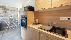 A modern kitchen with wooden cabinets, a built-in oven, a microwave, and a sink. - Galene - Appt avec jardin à 700 m de la Plage (Courseulles-sur-Mer)