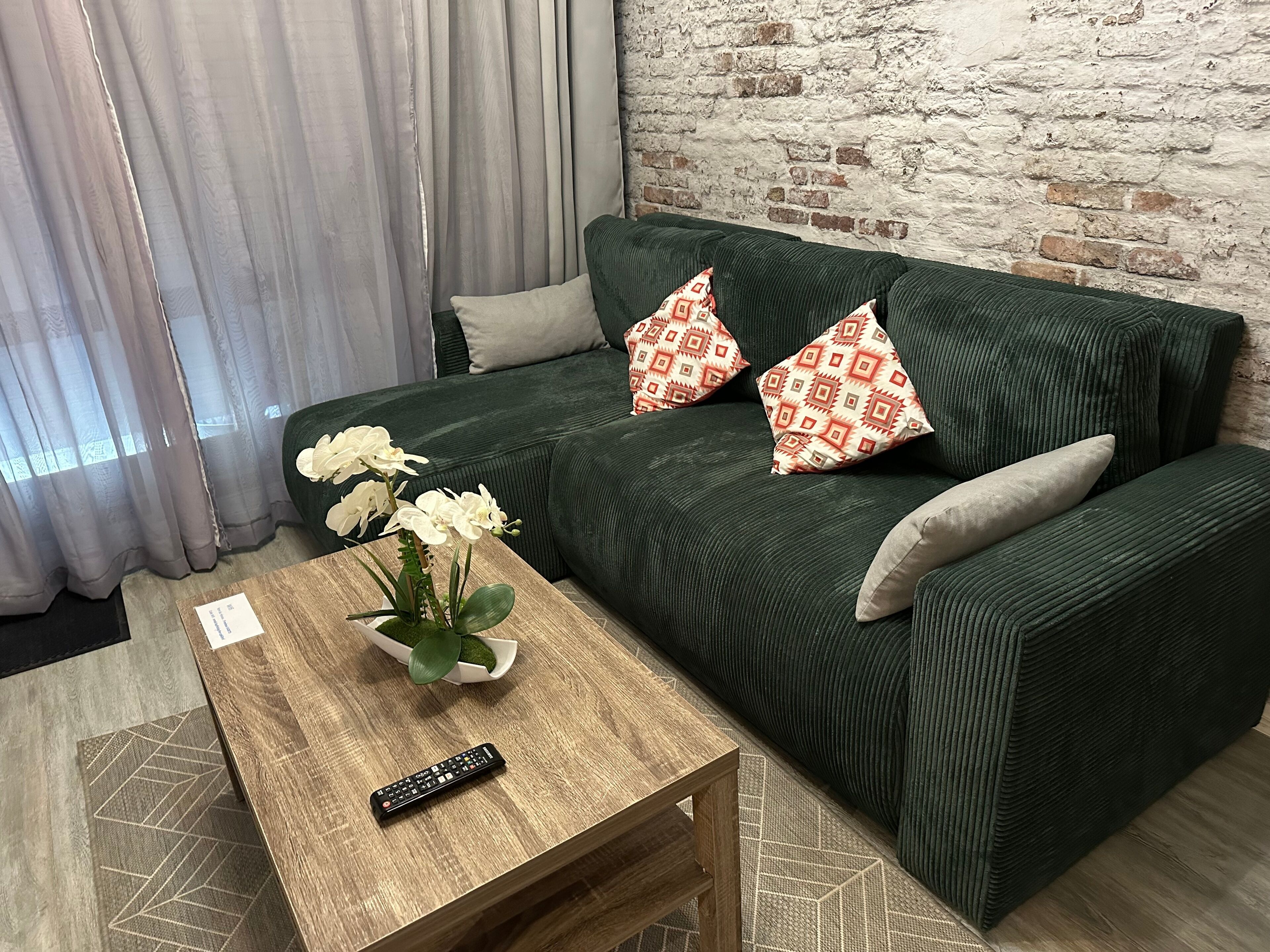 Un sofá verde con almohadones estampados, una mesa de centro de madera con un control remoto y orquídeas blancas.