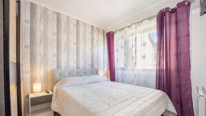 A bedroom with a bed, nightstand, and a window with curtains. - Galene - Appt avec jardin à 700 m de la Plage (Courseulles-sur-Mer)