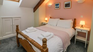 Une chambre avec un plafond en pente, un puits de lumière, un lit avec du linge de maison blanc, deux lampes de chevet et une tête de lit en bois.