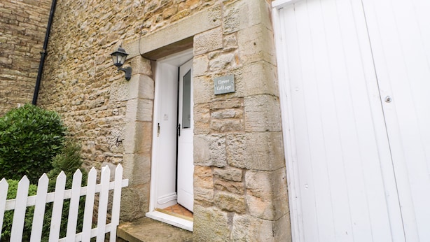 Une petite maison en pierre avec une porte blanche et une enseigne indiquant « Clover Cottage ».