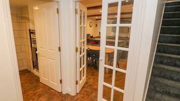 A hallway with a staircase, a dining area with chairs and a table, and a kitchen area with cabinets and a clock.