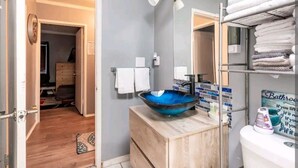 A bathroom with a wooden vanity, a blue glass sink, a towel rack, and a mirror.