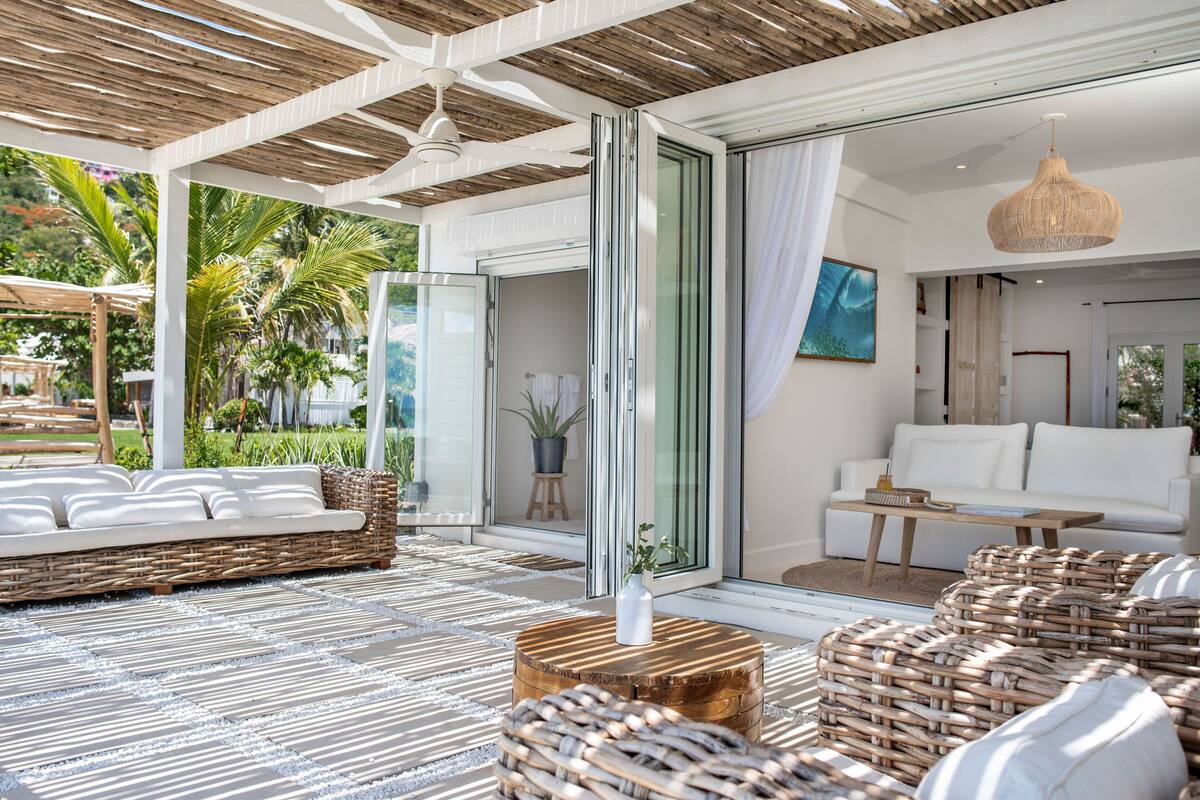 A modern outdoor lounge area with a wicker sofa, a round wooden table, and a wicker chair.