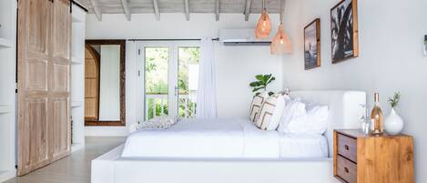 A spacious bedroom with a large bed, wooden wardrobe, and a view of greenery outside.