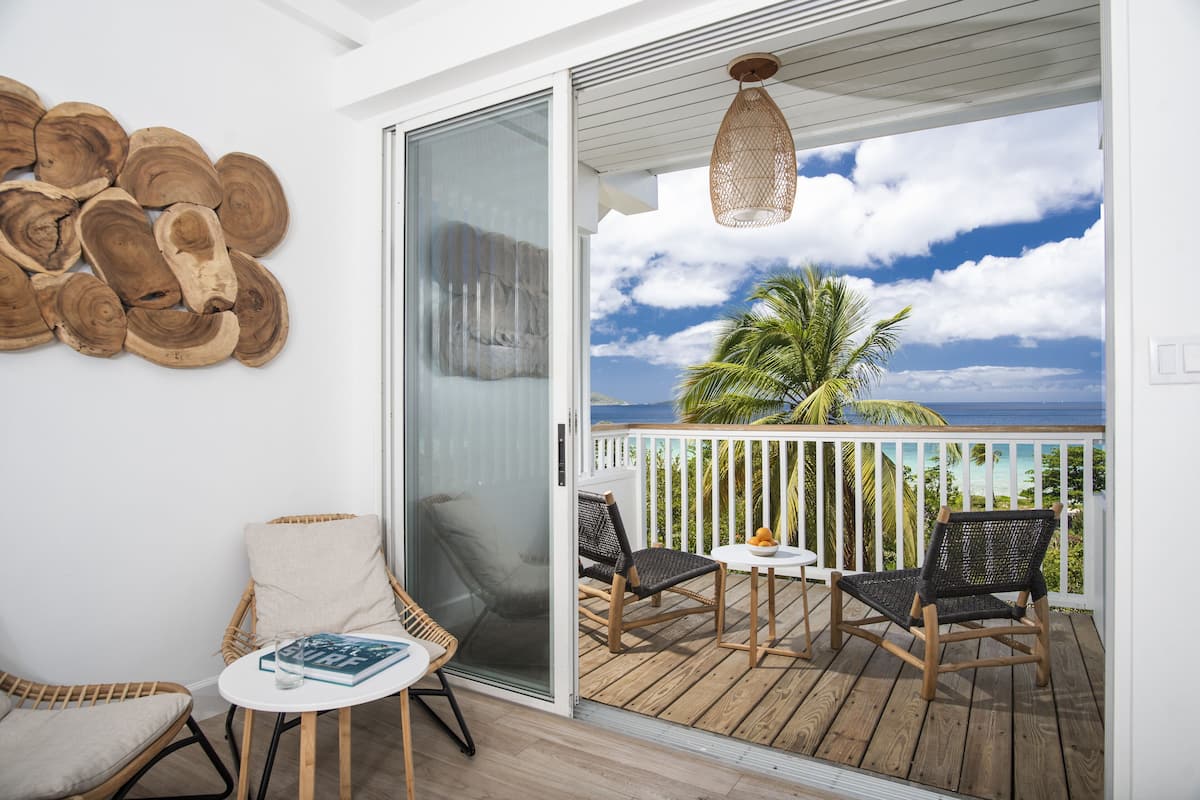 A balcony with wicker chairs, a small table, and a view of the ocean.