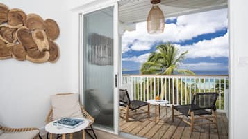 A balcony with wicker chairs, a small table, and a view of the ocean.