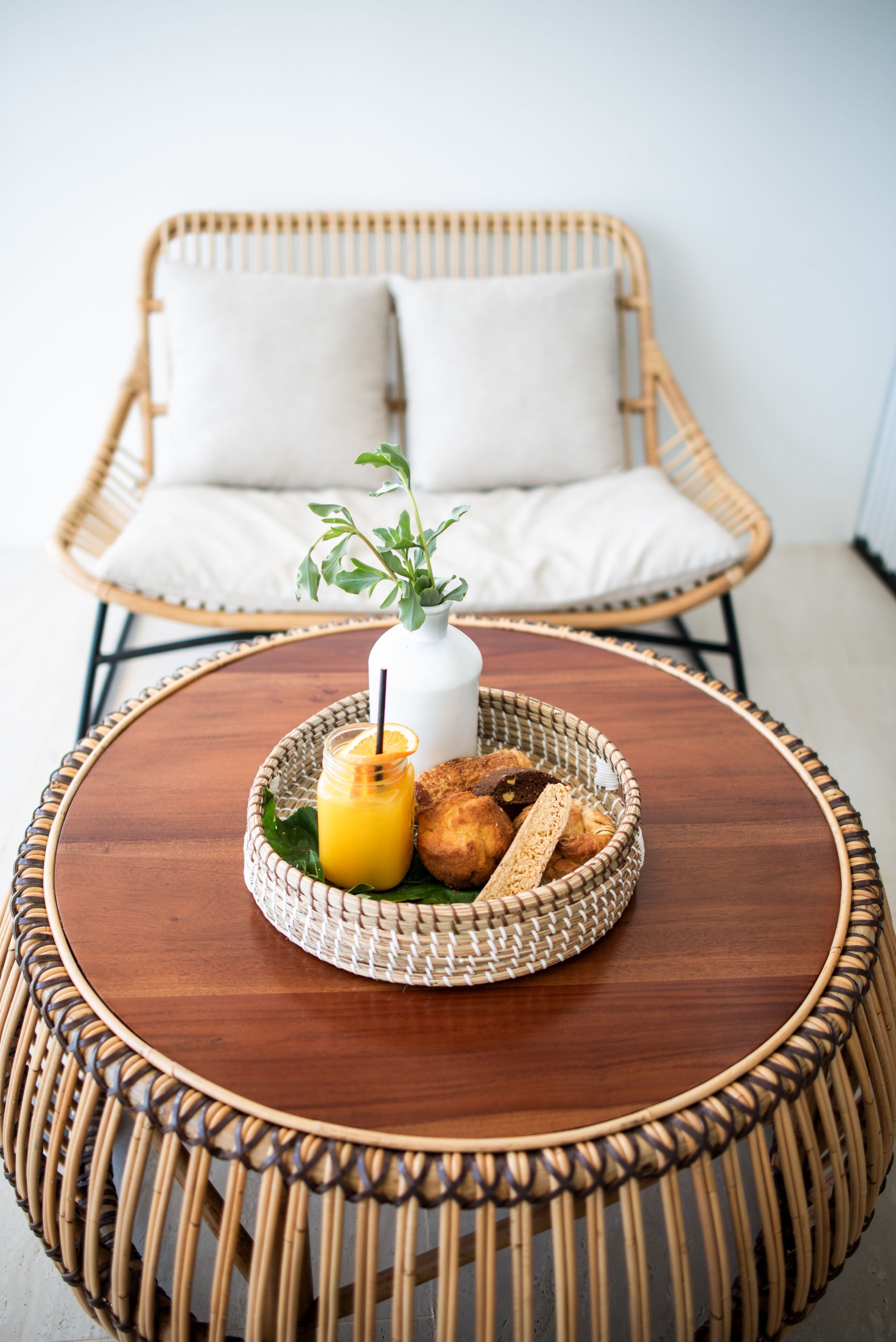 A wicker round table with a white vase, a glass of orange juice, and bread.