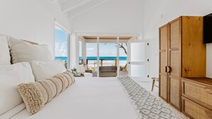 A bedroom with a large bed, a wooden wardrobe, and a view of the beach through an open door. - Long Bay Beach Resort (West End)