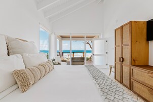 Quarto com uma cama grande, um guarda-roupa de madeira e vista para a praia através de uma porta aberta.