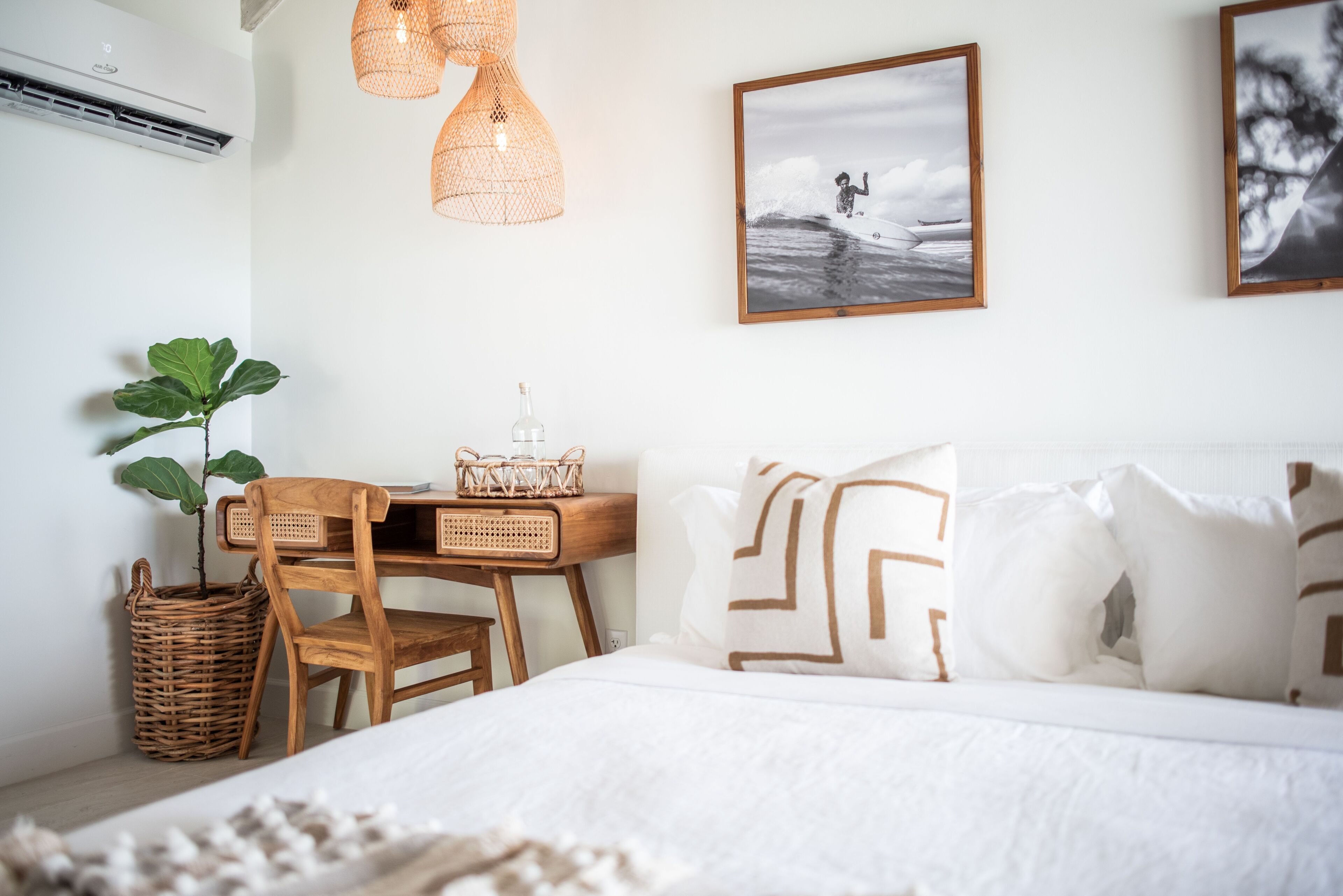 Un dormitorio con cama, escritorio de madera, mobiliario de mimbre y una obra de arte en la pared.