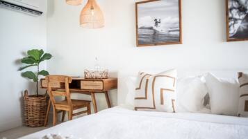 Un dormitorio con cama, escritorio de madera, mobiliario de mimbre y una obra de arte en la pared.