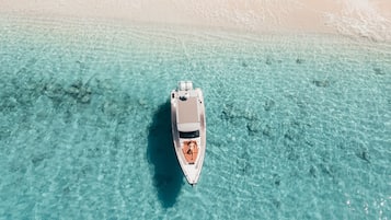 Un yacht sur une eau turquoise et limpide, avec une plage de sable en arrière-plan.