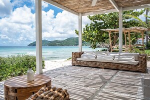 Espaço de estar coberto ao ar livre, com sofá de vime e mesa redonda, com vista para a praia e o oceano.