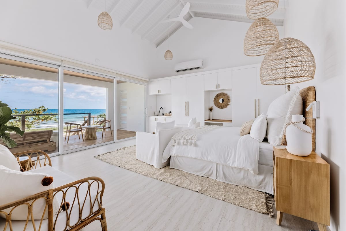 A modern bedroom with a large bed, white furniture, and a view of the ocean.