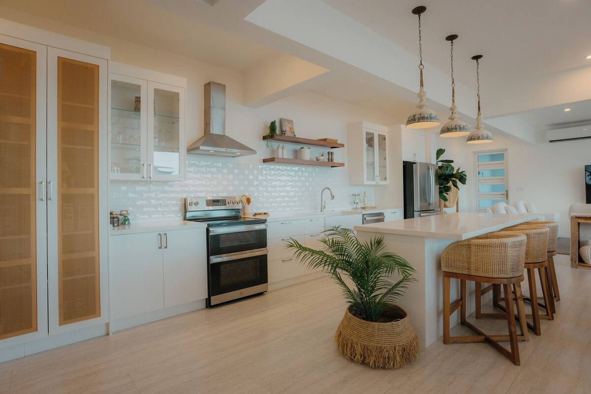 A modern kitchen with white cabinetry, a central island with bar stools, a built-in oven, and pendant lighting.