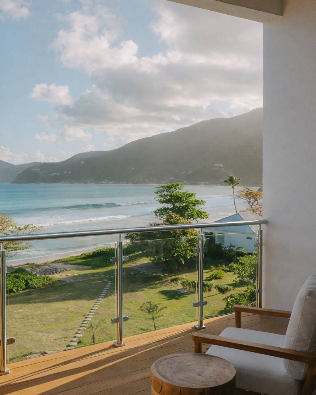 A balcony with a view of the ocean and hills, a wooden deck, and a white chair.