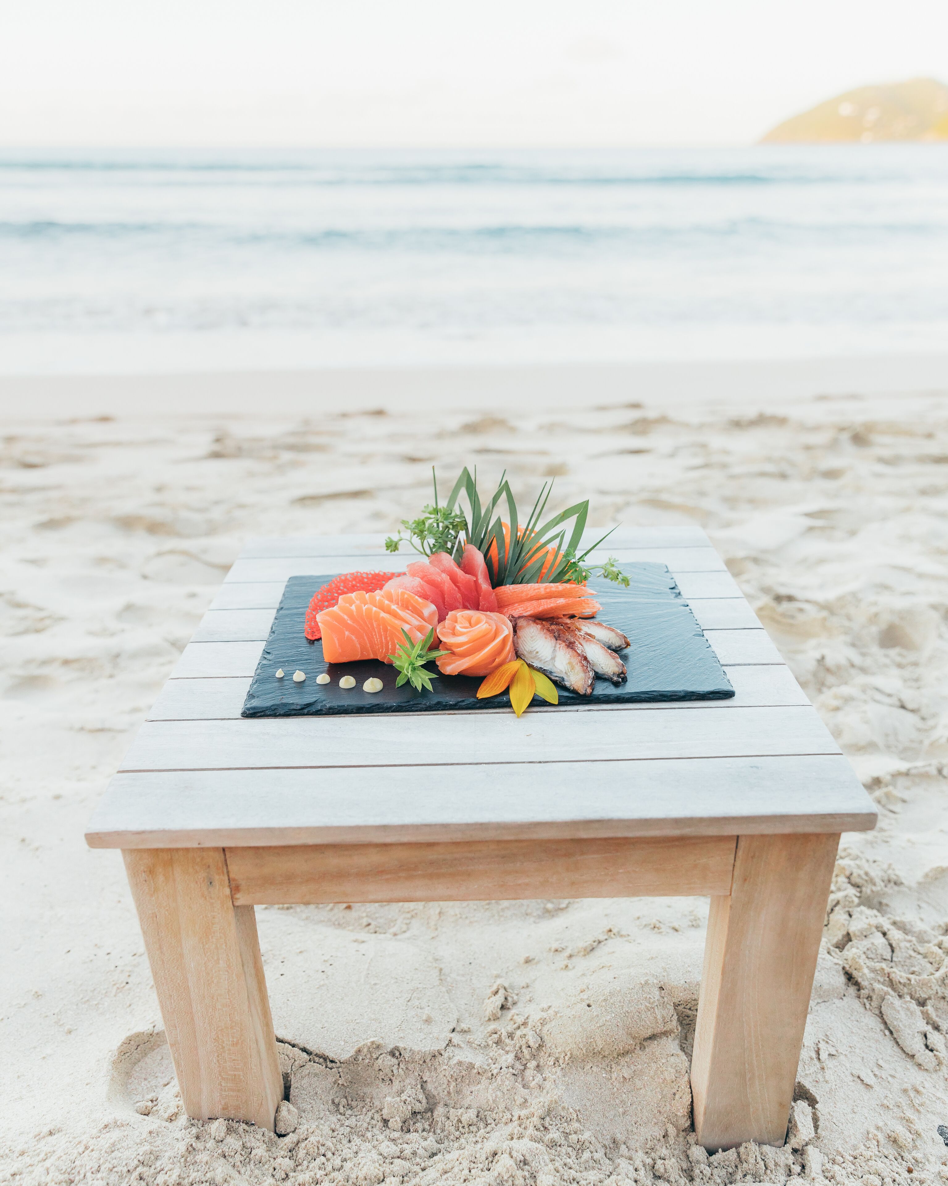 Una mesa de madera con superficie de pizarra negra en una playa arenosa.