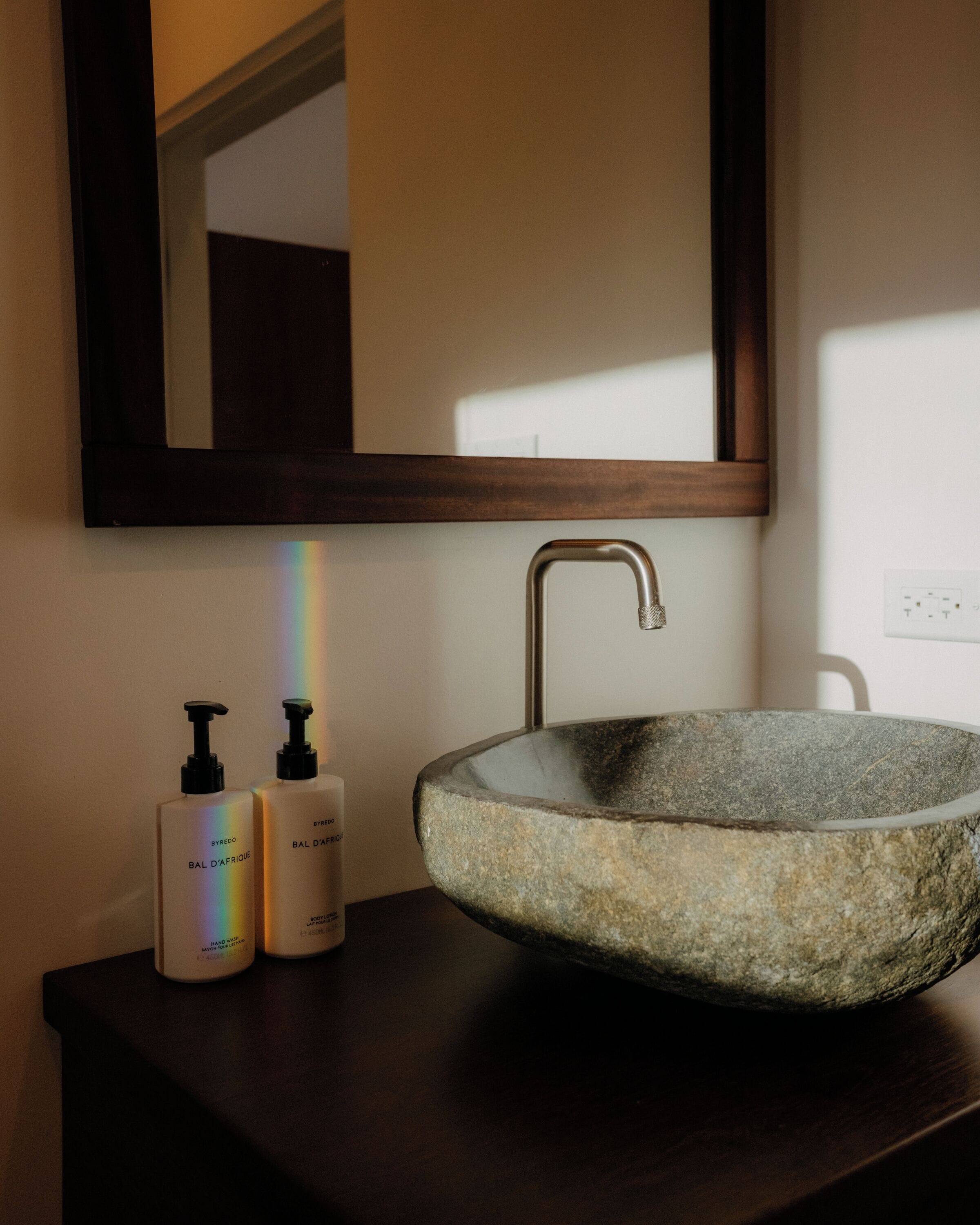 A bathroom with a stone sink, a mirror, and two hand sanitizer bottles.