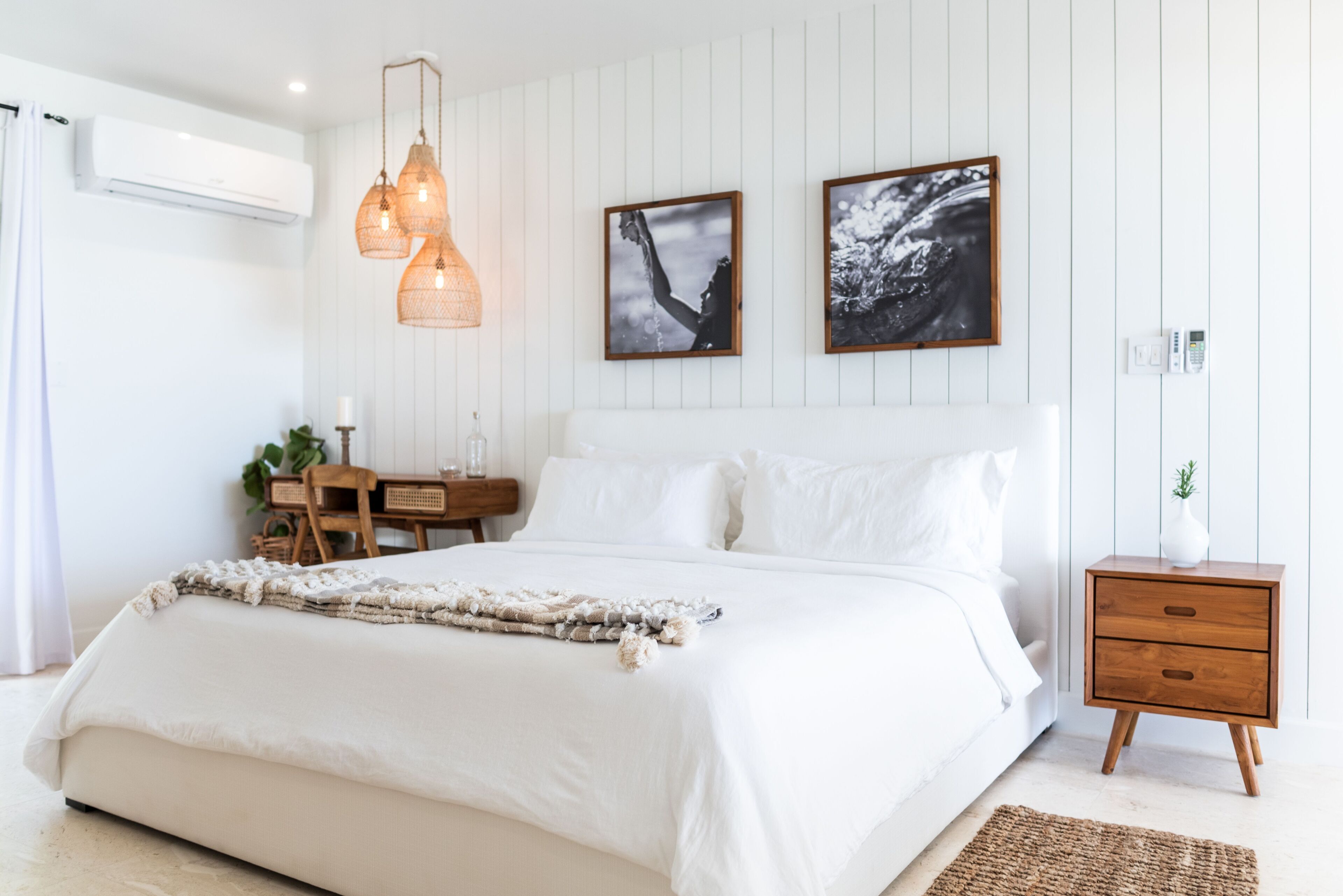 A bedroom with a large bed, a wooden nightstand, a desk with a chair, and two wall-mounted pendant lights.