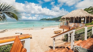 A beachside view with a thatched-roof structure, wooden deck, and sandy beach. - Long Bay Beach Resort (West End)