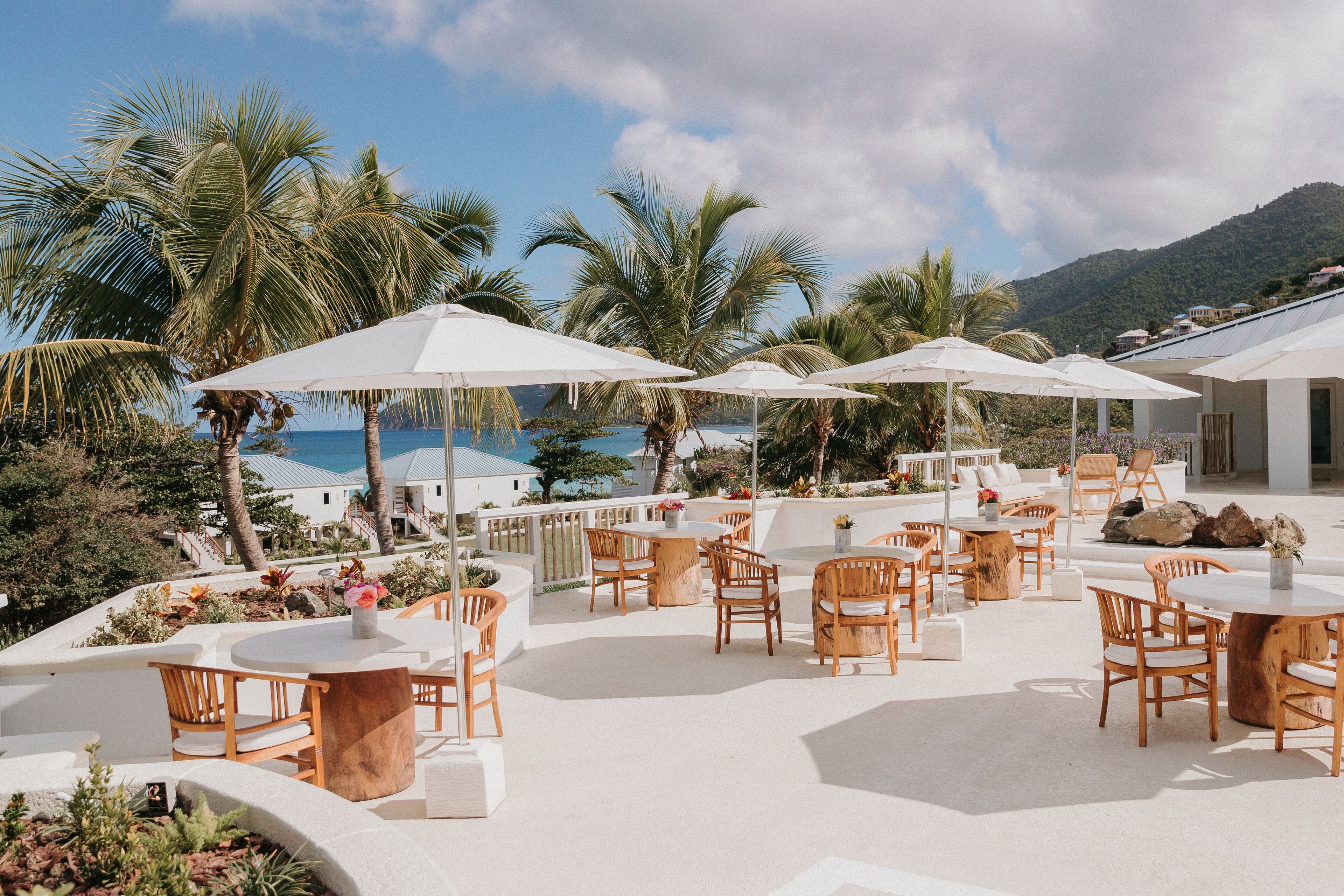 A rooftop terrace with outdoor seating, palm trees, and a view of the ocean.