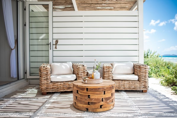 A wicker sofa set with white cushions, a wooden coffee table, and a glass door leading to a beach view. - Long Bay Beach Resort (West End)