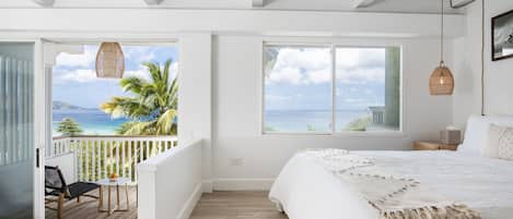 A bedroom with a large bed, a balcony with a view of the ocean, and a hanging light fixture.