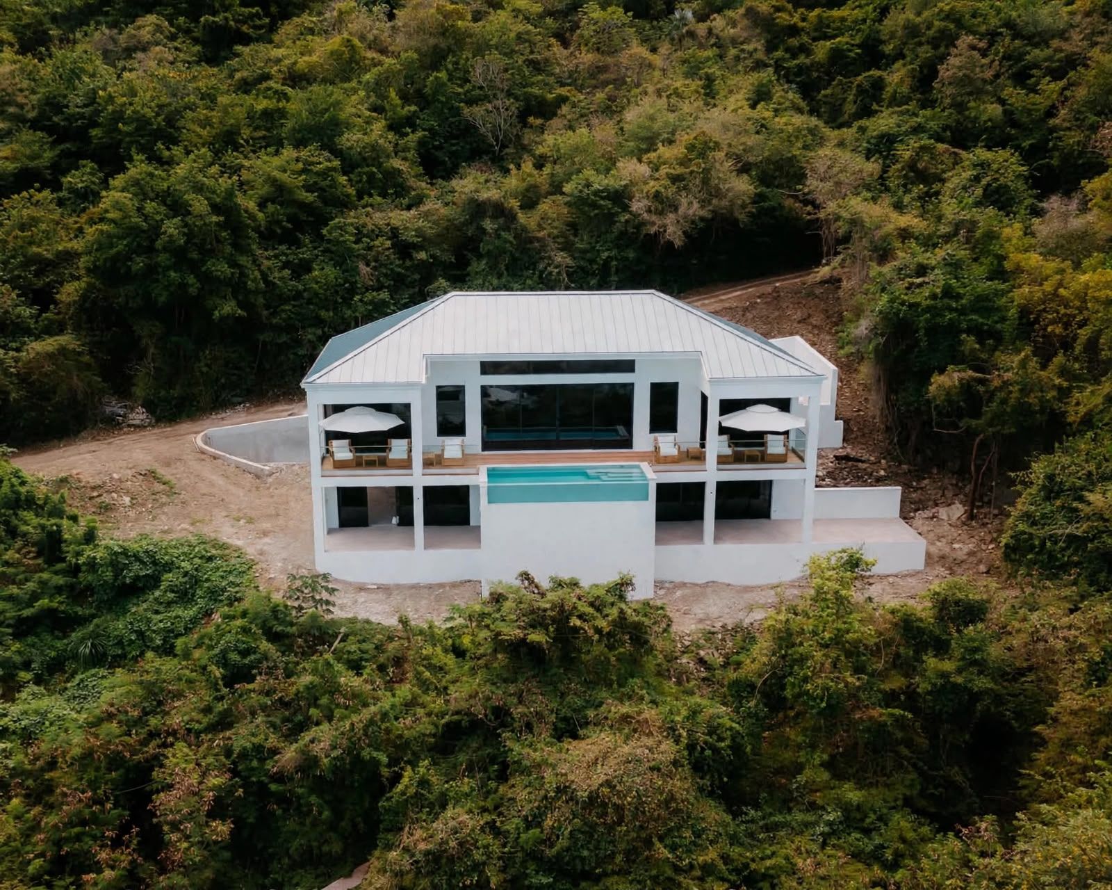 A modern two-story house with a swimming pool, surrounded by dense forest.