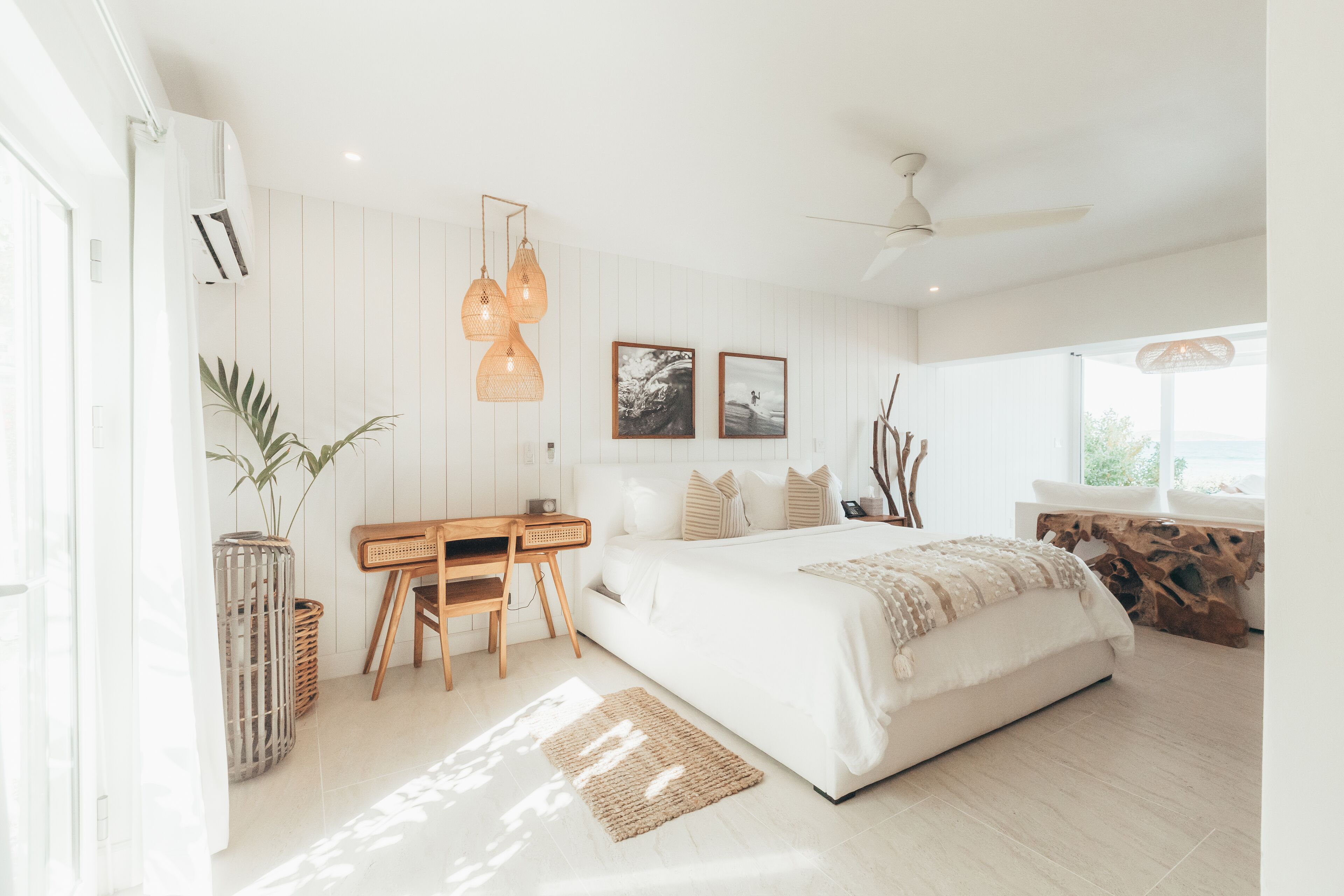 A modern bedroom with a large bed, a desk, and a view of the outdoors.