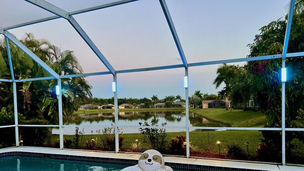 A pool with a large inflatable dog float, surrounded by a glass enclosure with views of a golf course and a lake. - Gorgeous Naples home with Saltwater pool in a gated community  (Naples)