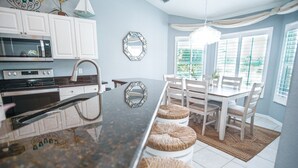 A kitchen with white cabinets, a microwave, an oven, and a dining area with a table and chairs. - Gorgeous Naples home with Saltwater pool in a gated community  (Naples)