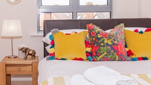 Una cama bien tendida con almohadas coloridas, una lámpara de noche y una pequeña figurita de elefante decorativa.
