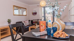 Un comedor con una mesa dispuesta para el desayuno, incluyendo un plato de pasteles, una caja de cereales Dorsett y un florero con una planta.