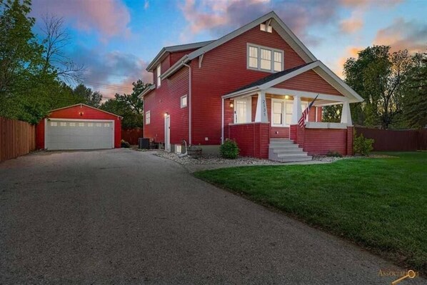 Une maison à deux étages, avec une façade rouge, un porche à l’avant et un garage.