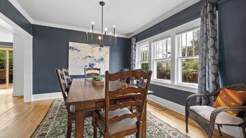 A dining room with a wooden table and chairs, a chandelier, and a large window with curtains.