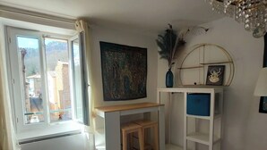 A room with a window, a desk, a chair, a shelf, and a decorative mirror. - Cosy T2 apartment with river view, sleeps 2 (Rennes-les-Bains)