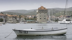Una pequeña embarcación con el registro TG-123 fondeada cerca de un puerto con edificios y una torre al fondo.
