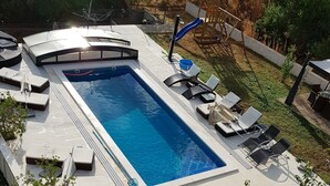 Una piscina rectangular con una terraza curva, rodeada de sillas de descanso y un tobogán.