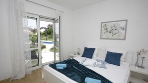Un dormitorio con cama, mesita de noche, ventana con cortinas y vista a una piscina.