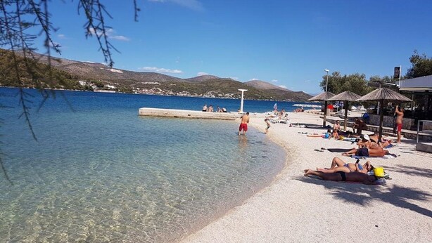 Una playa con agua cristalina, gente tomando el sol y un muelle.