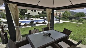 Un área de estar al aire libre, techada, con una piscina al fondo.