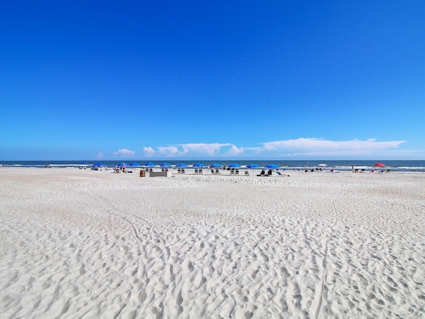 A wide sandy beach with several umbrellas and beach chairs.
