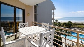 Varanda com mesa e cadeiras, com vista para a praia e uma piscina.