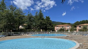 A swimming pool with lounge chairs and a stone deck, surrounded by trees and buildings. - Villa Jolymelody (Santa-Maria-Poggio)