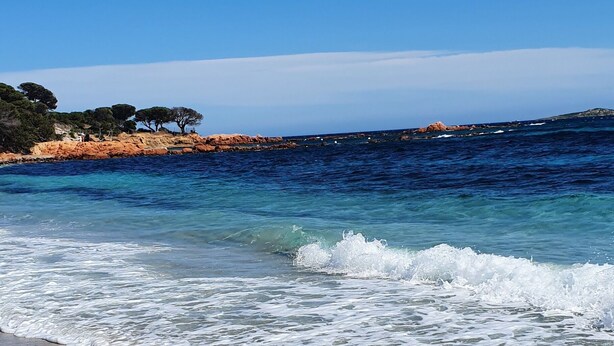 A beach with clear blue water, sandy shore, and rocky cliffs in the background. - Villa Jolymelody (Santa-Maria-Poggio)
