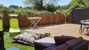 A wooden deck with outdoor furniture, including a table and chairs, surrounded by a wooden fence and greenery. - Villa Jolymelody (Santa-Maria-Poggio)