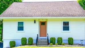 A single-story house with a brown front door, white siding, and a brown roof. There are six windows, two on each side of the door, and a small porch with steps leading to the door. - Create Memories at our Modern Waterfront 1 BR Apartment: Hike, Sip Wine, Relax!  (Wallkill)