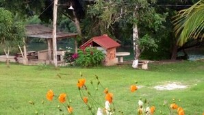 A garden with a small red-roofed structure, a wooden bench, and various plants and flowers. - Aliana's Villas - Private Farm Home on the River (Gold Standard Certified) (San Ignacio)